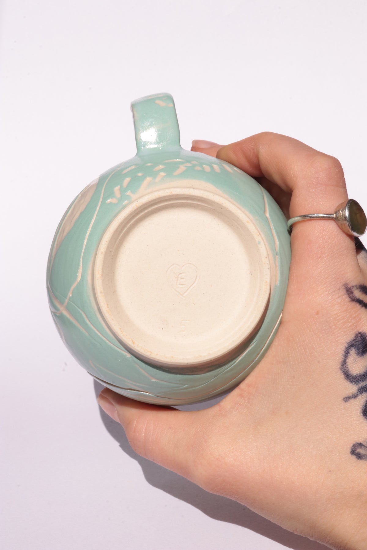 Teal mug with engraved white abstract design on a white background
