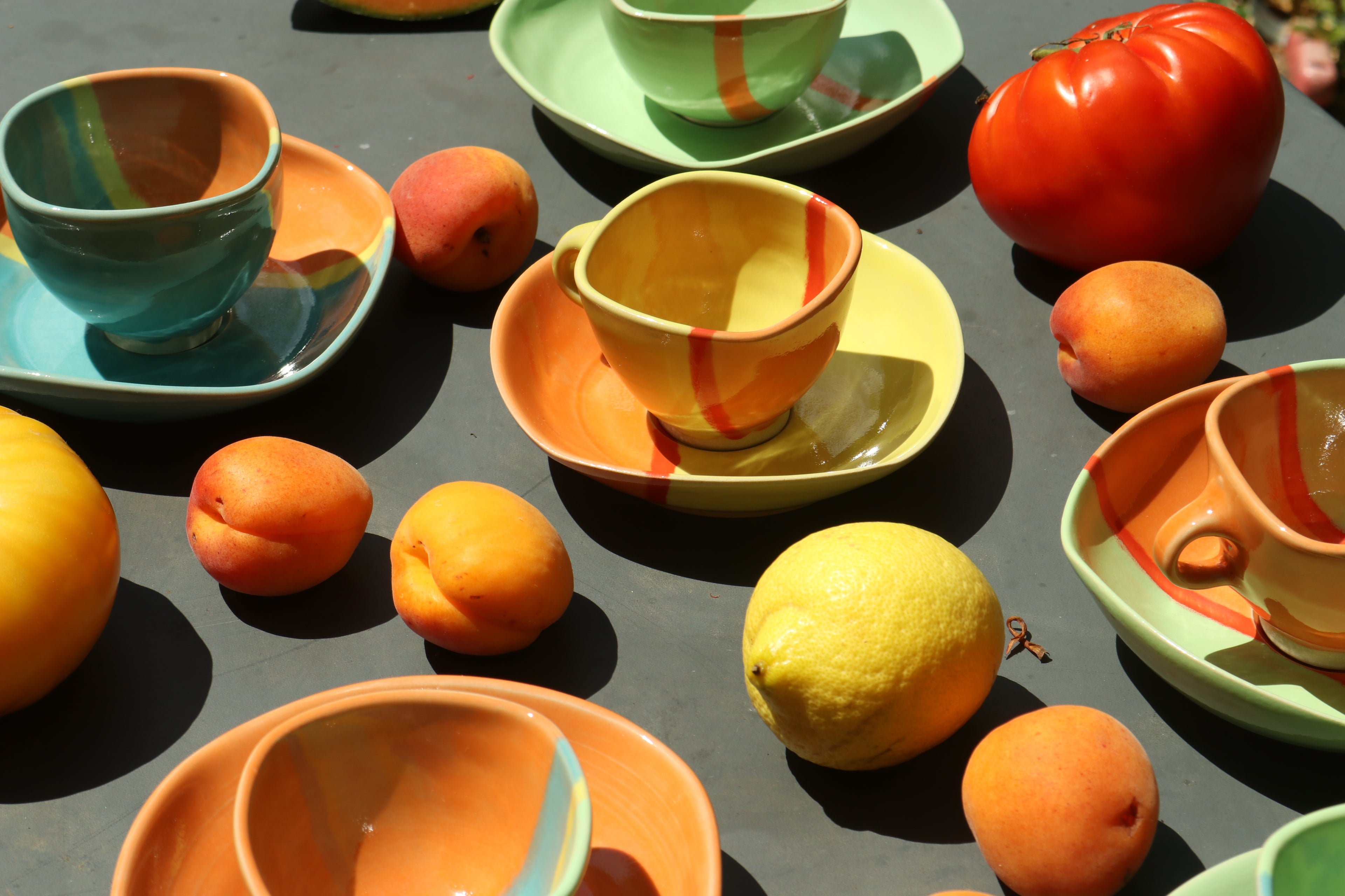 Colorful ceramic cups and saucers with fruits on a dark surface