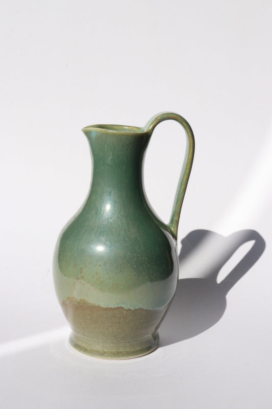 Green ceramic jug with elegant curves and hand pulled handle on a white background