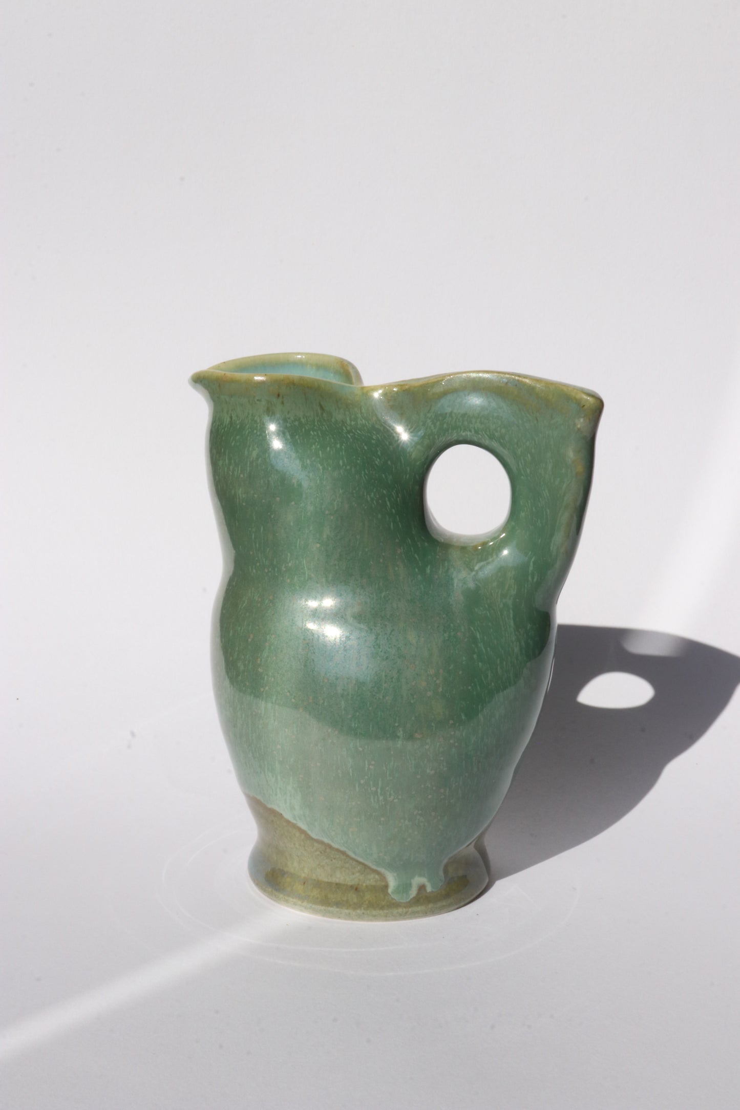 Green ceramic jug with a hole  for a handle on a white background