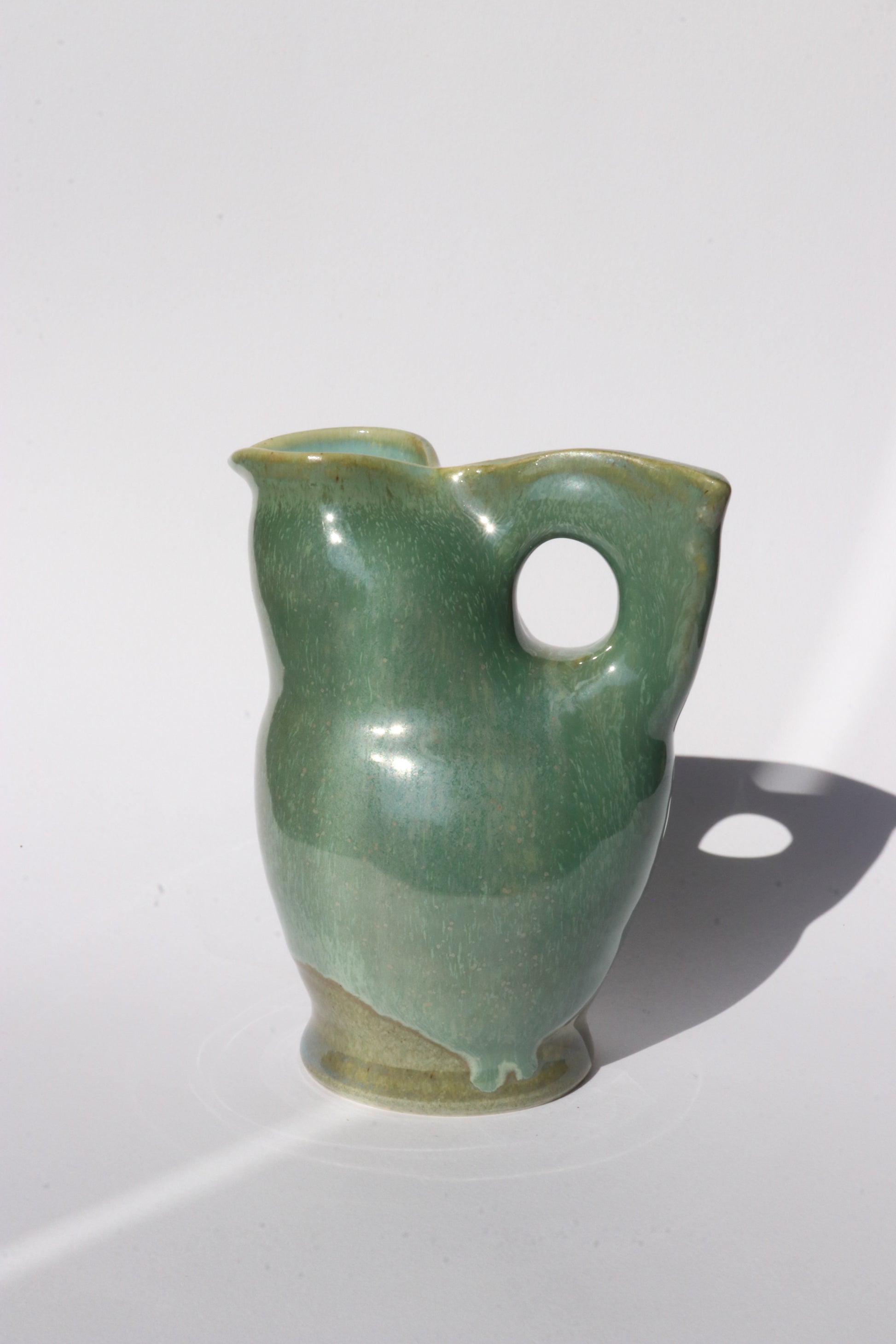Green ceramic jug with a hole  for a handle on a white background
