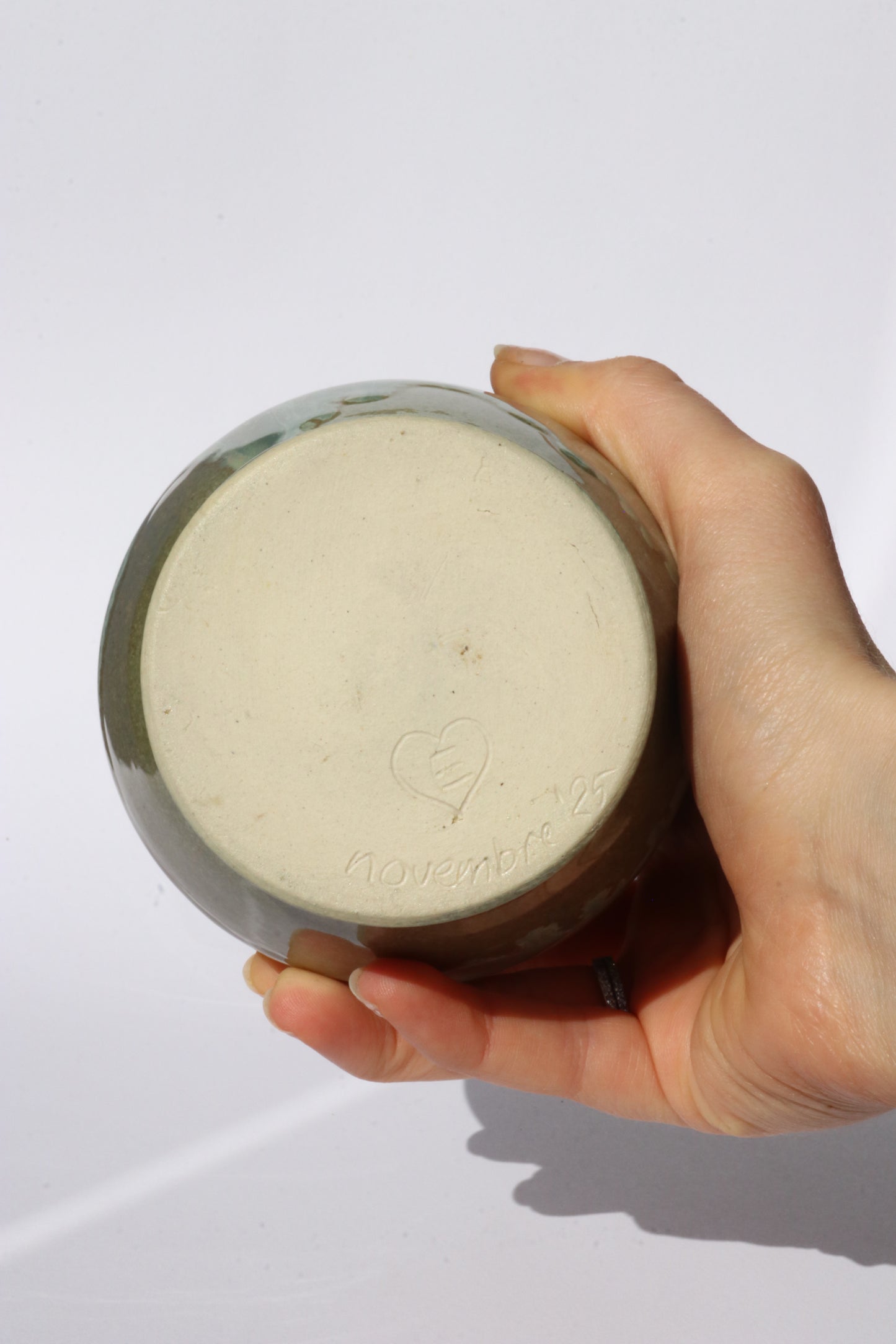 hand holding bottom of ceramic green jug, showing the signature