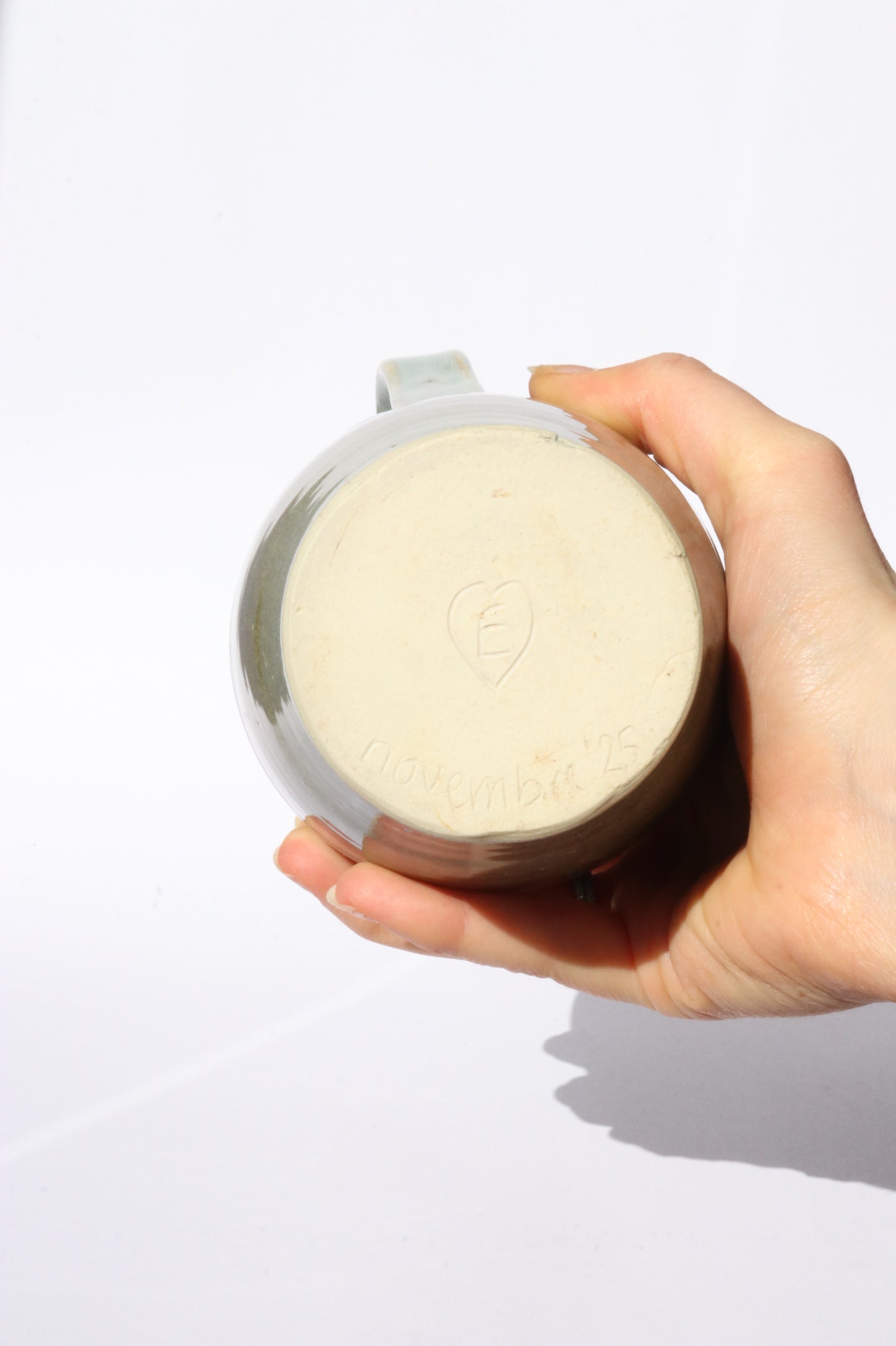 Hand holding green ceramic jug showing the signed bottom against a white background