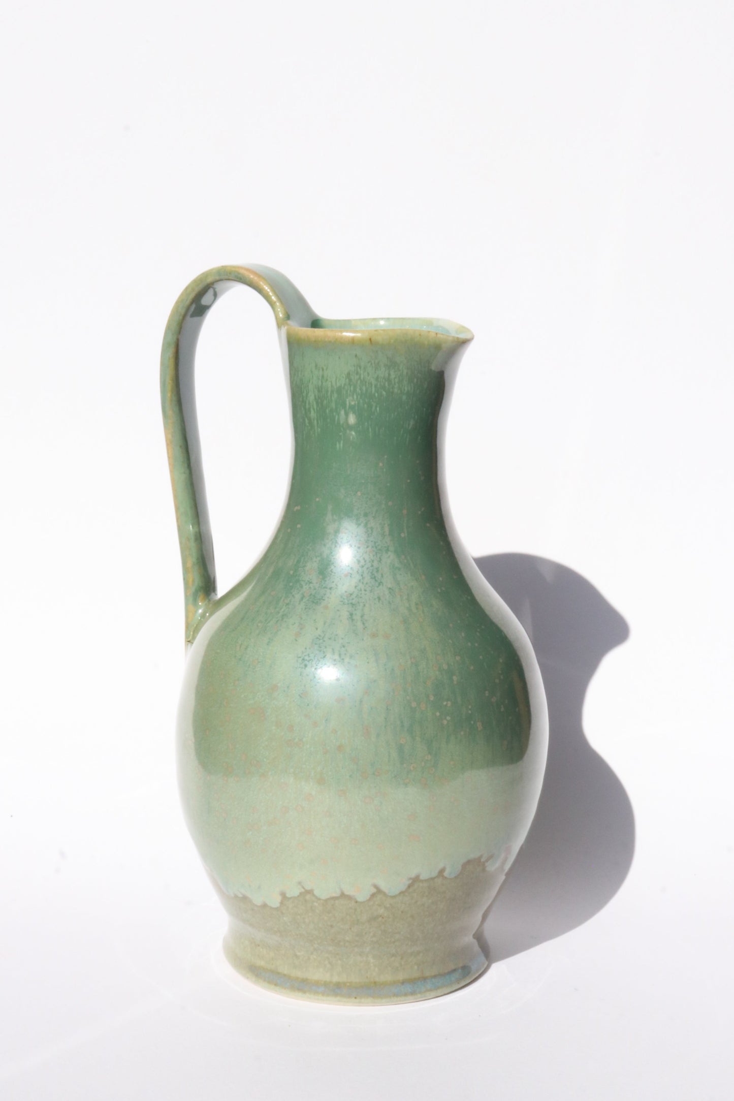 green ceramic jug with elegant curves and handle on white background