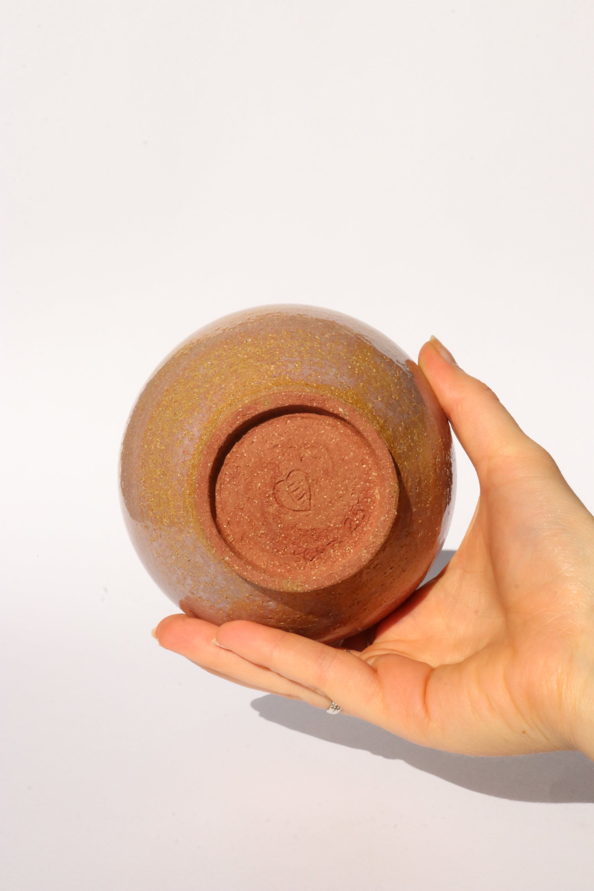 Hand holding a ceramic bowl showing the signature at the bottom