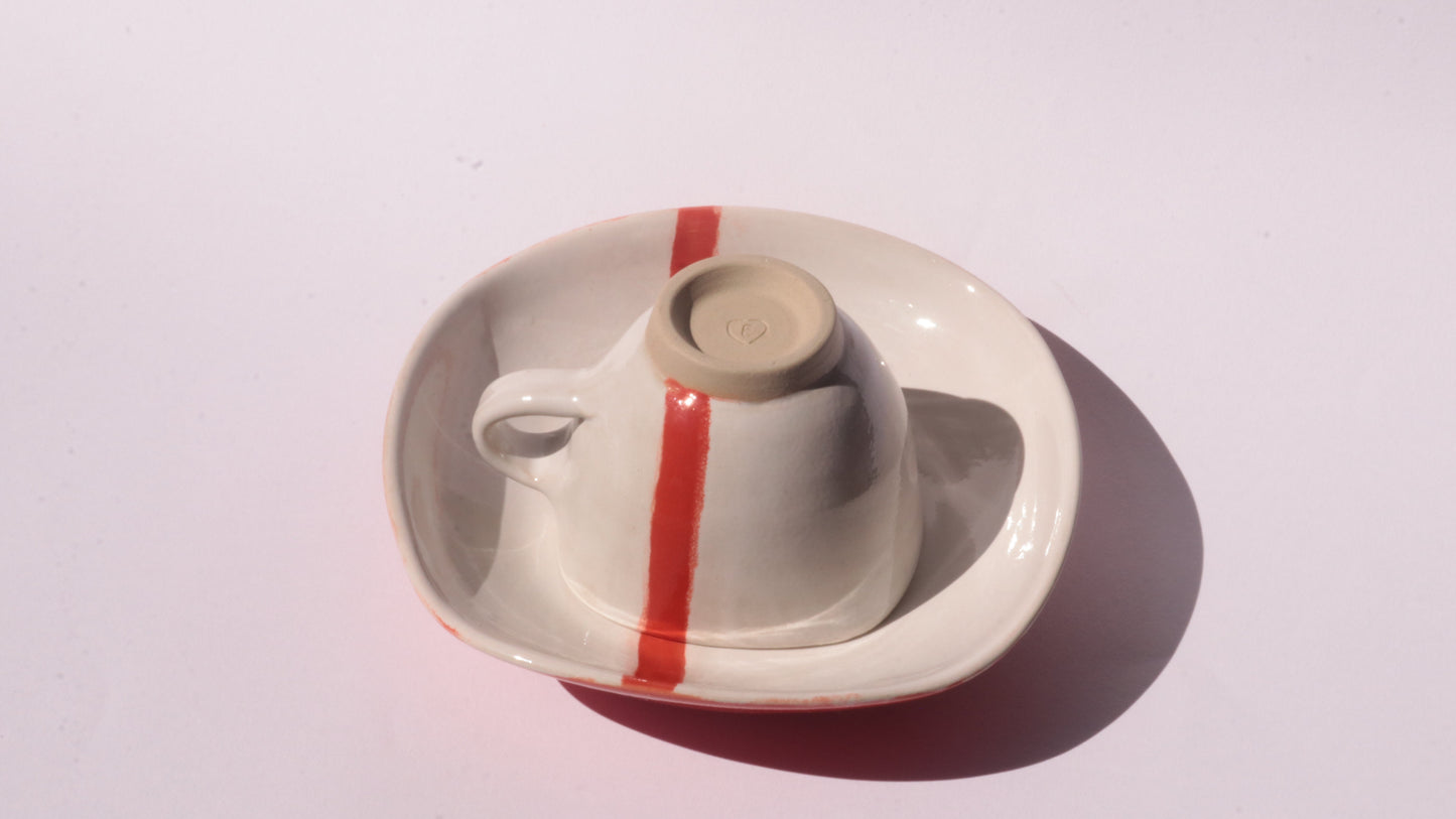 Ceramic cup and saucer with a red stripe on a white background