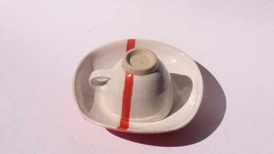 Ceramic cup and saucer with a red stripe on a white background