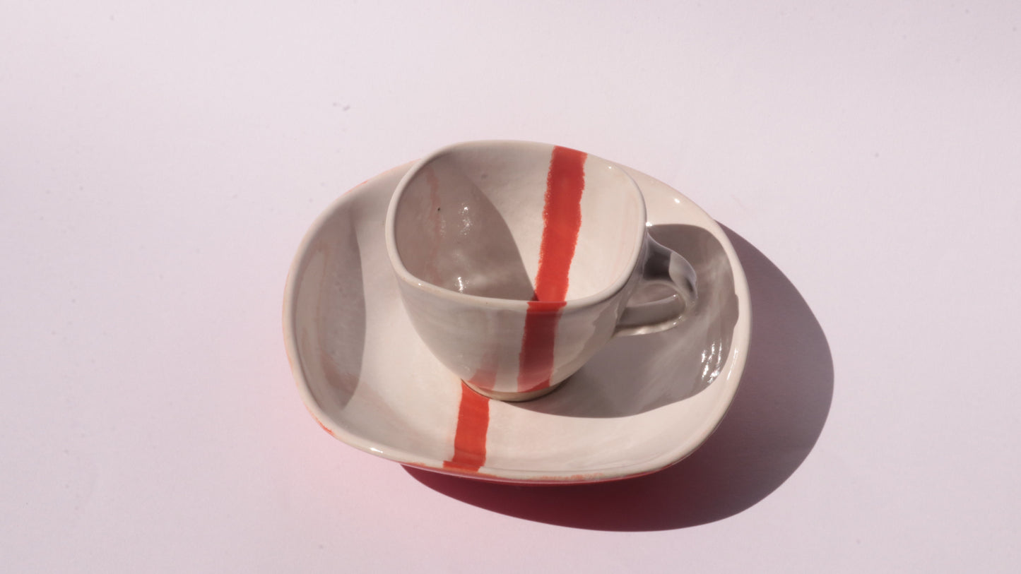 Ceramic cup and saucer with a red stripe on a white background