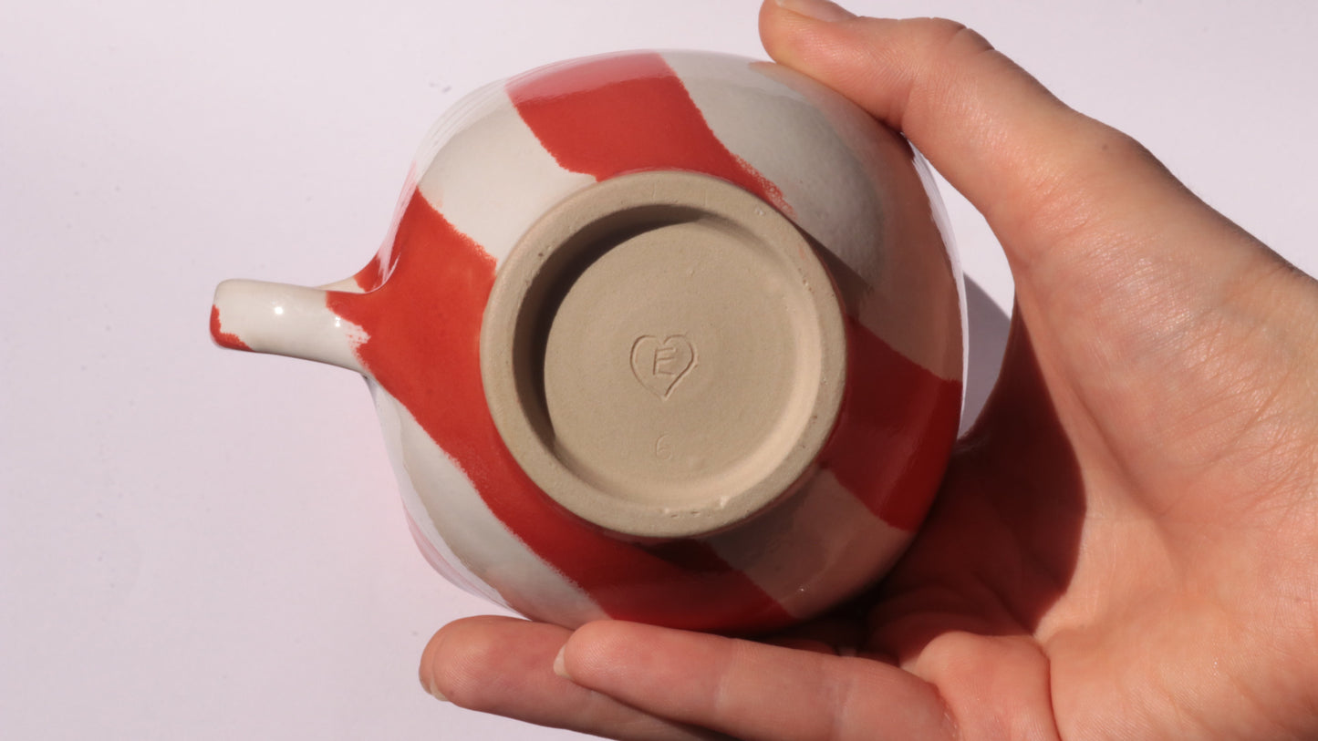hand holding signed red and white striped ceramic cup on white background