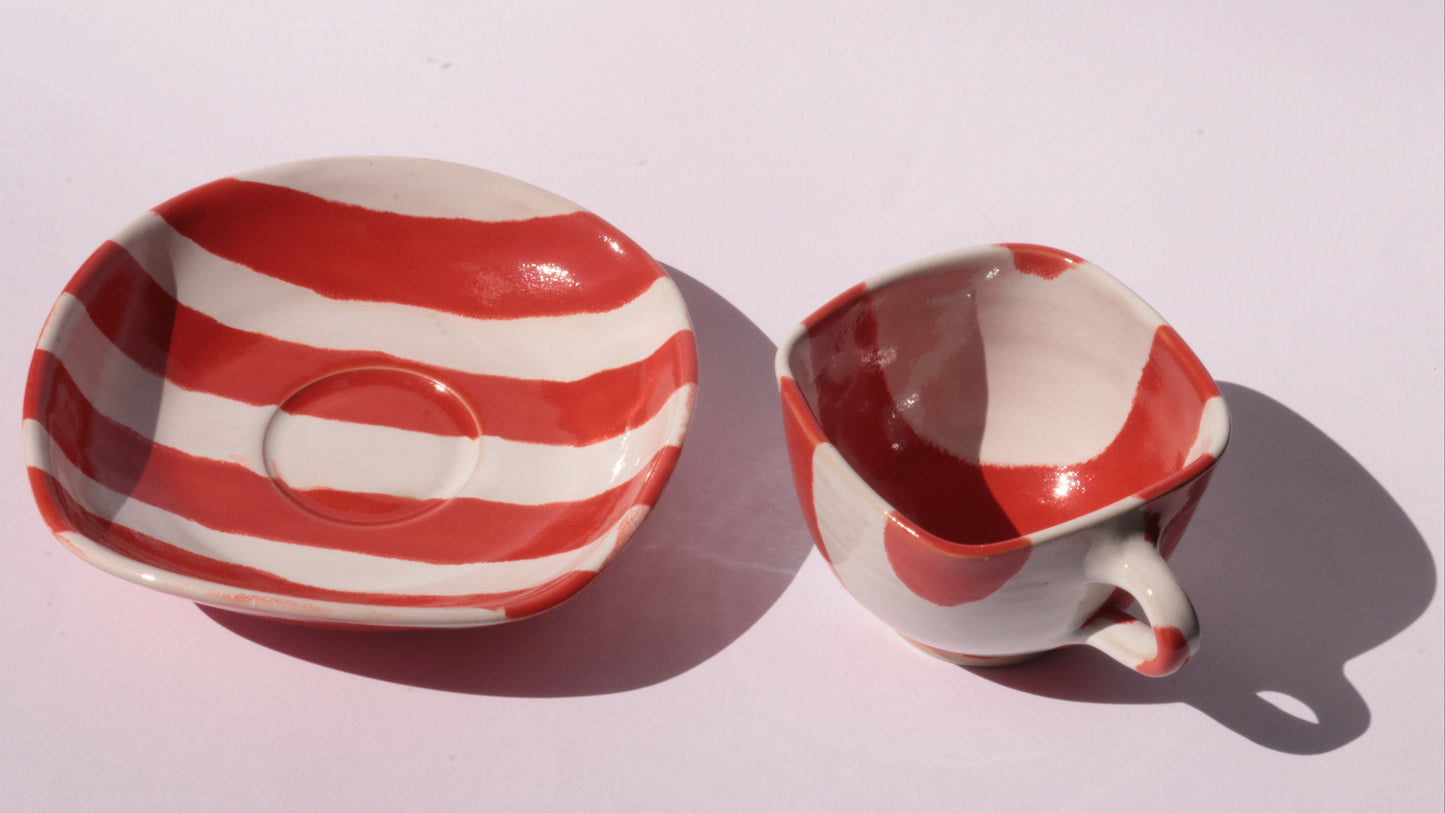 red and white striped ceramic cup and saucer on white background