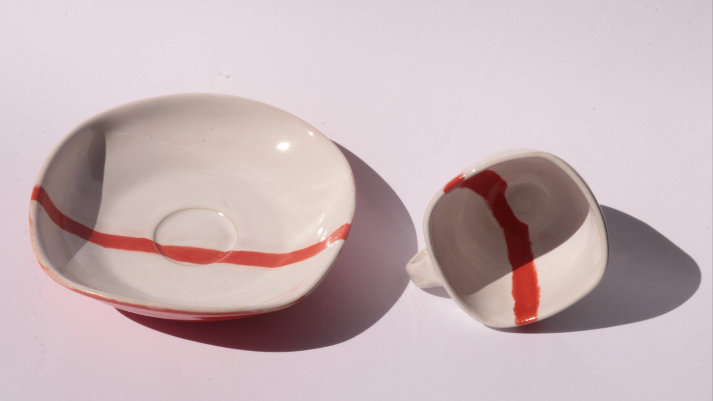 Ceramic cup and saucer with a red stripe on a white background