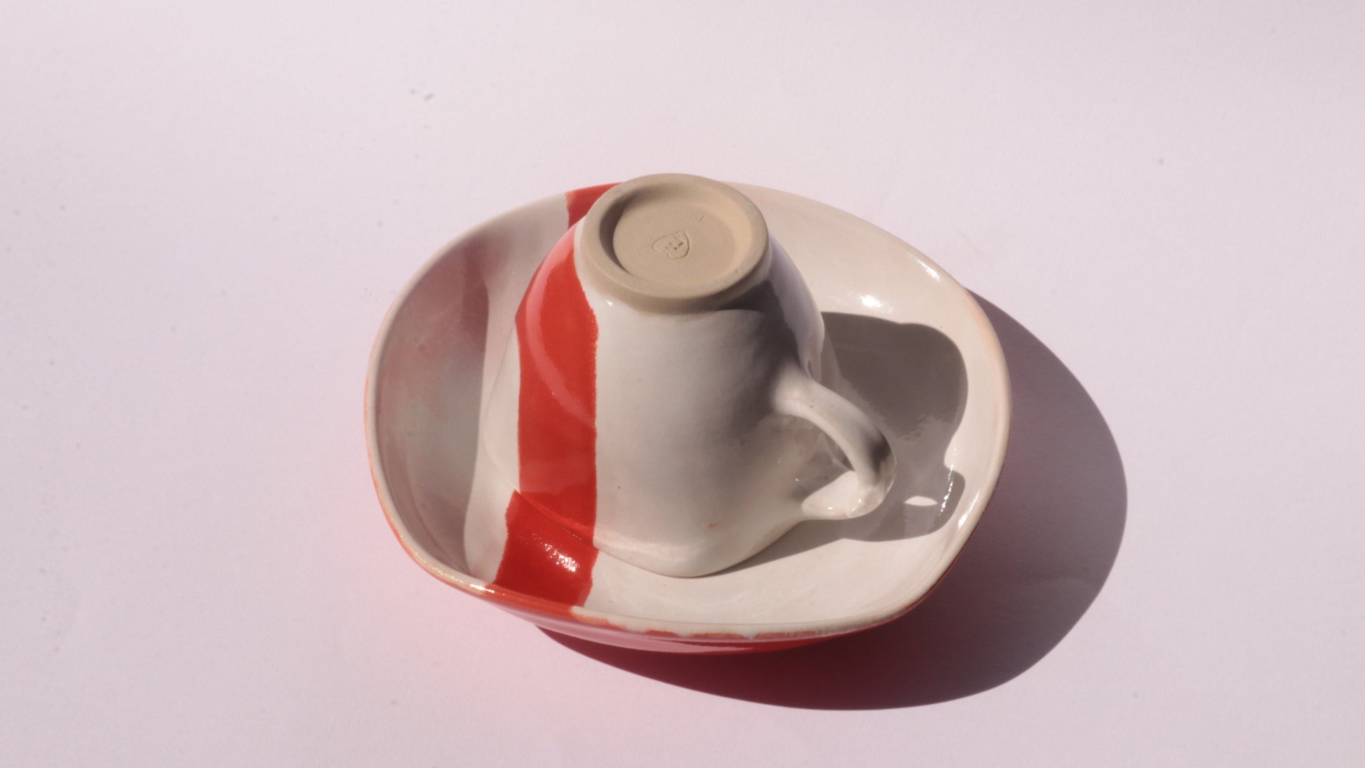 Ceramic cup and saucer with thick red stripe on a white background