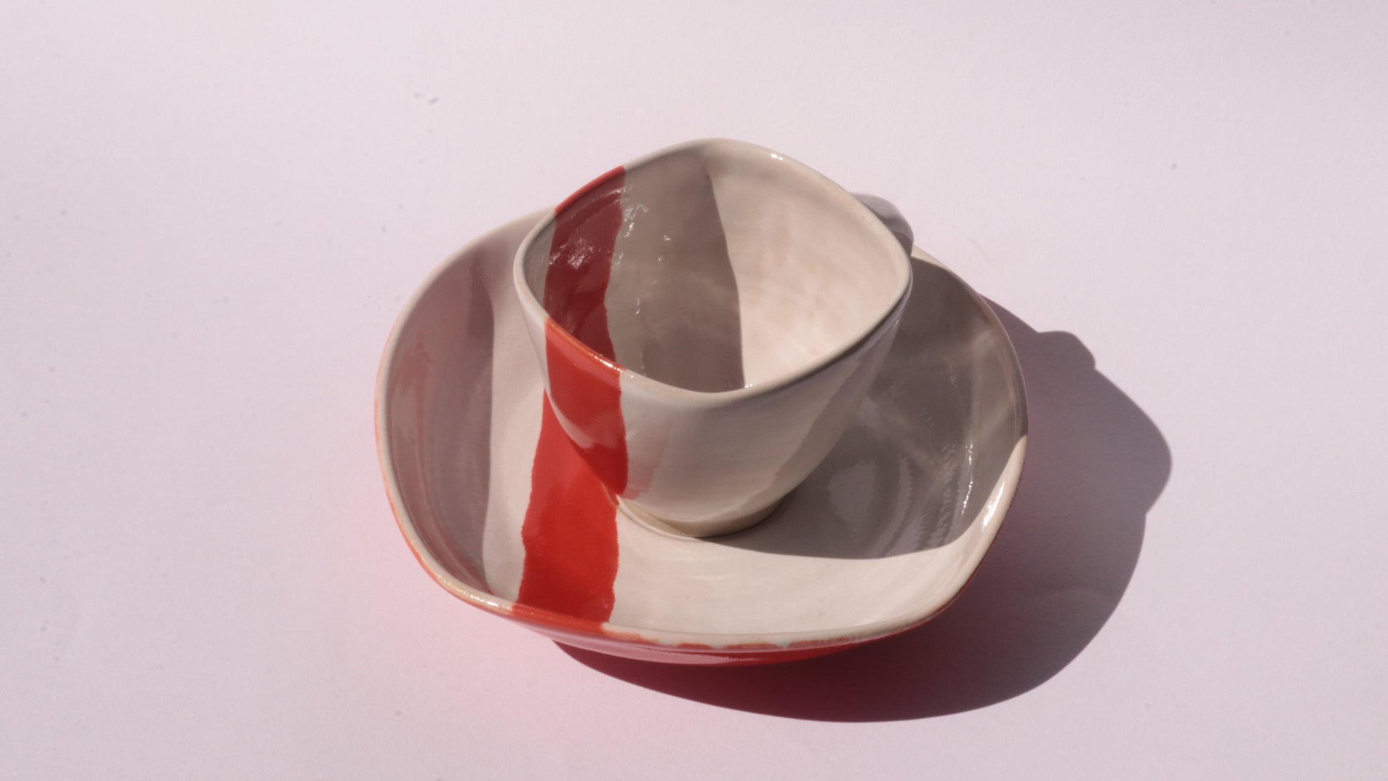 Ceramic cup and saucer with thick red stripe on a white background