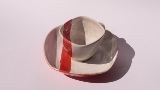 Ceramic cup and saucer with thick red stripe on a white background