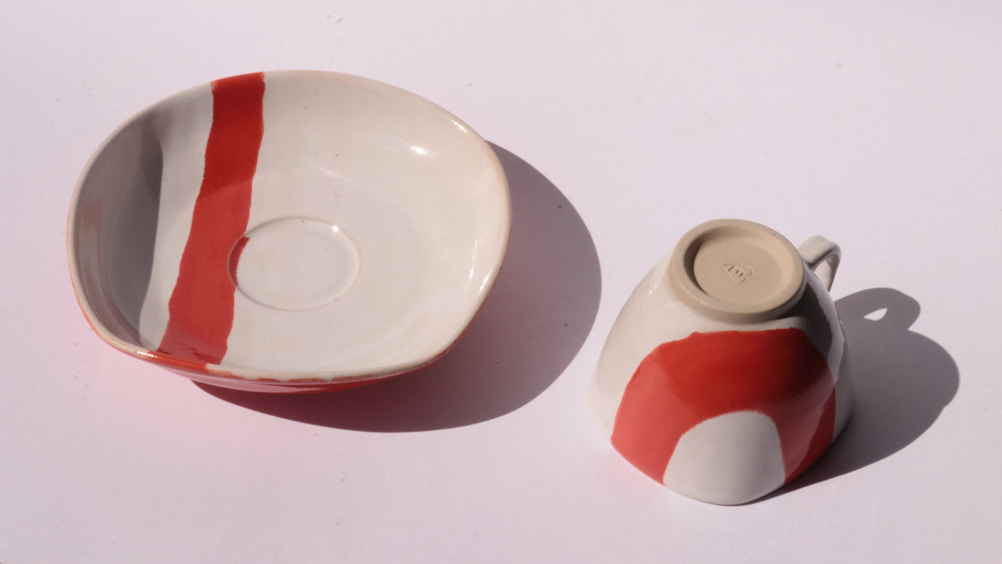 Ceramic cup and saucer with thick red stripe on a white background