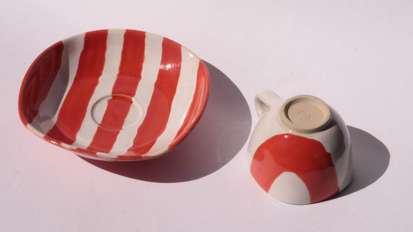 Ceramic cup and saucer with red and white stripes on a white background