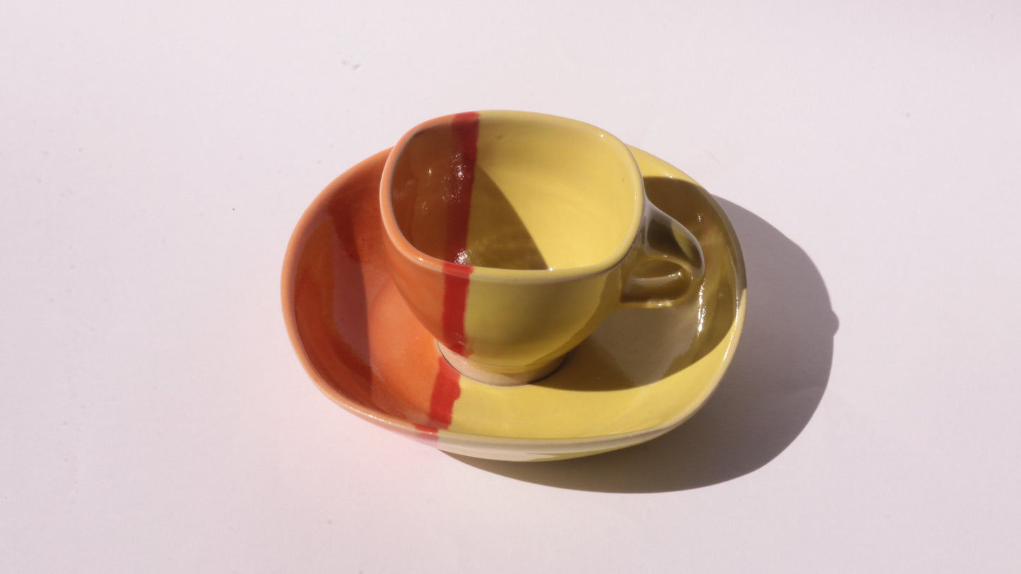Yellow ceramic cup and saucer with red and orange stripes on a white background