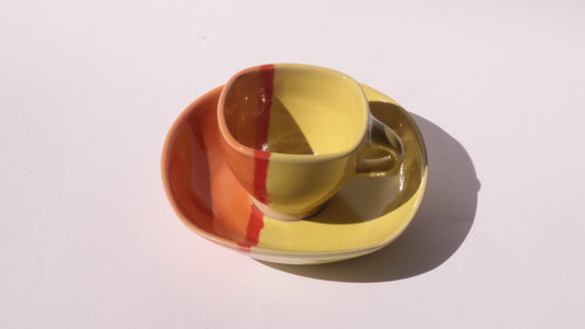 Yellow ceramic cup and saucer with red and orange stripes on a white background