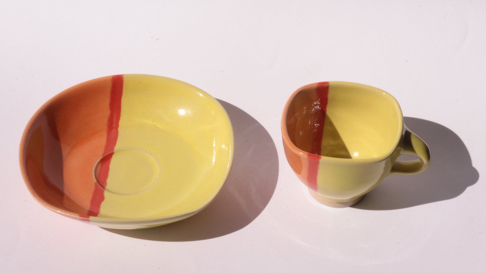 Yellow ceramic cup and saucer with red stripes on a white background