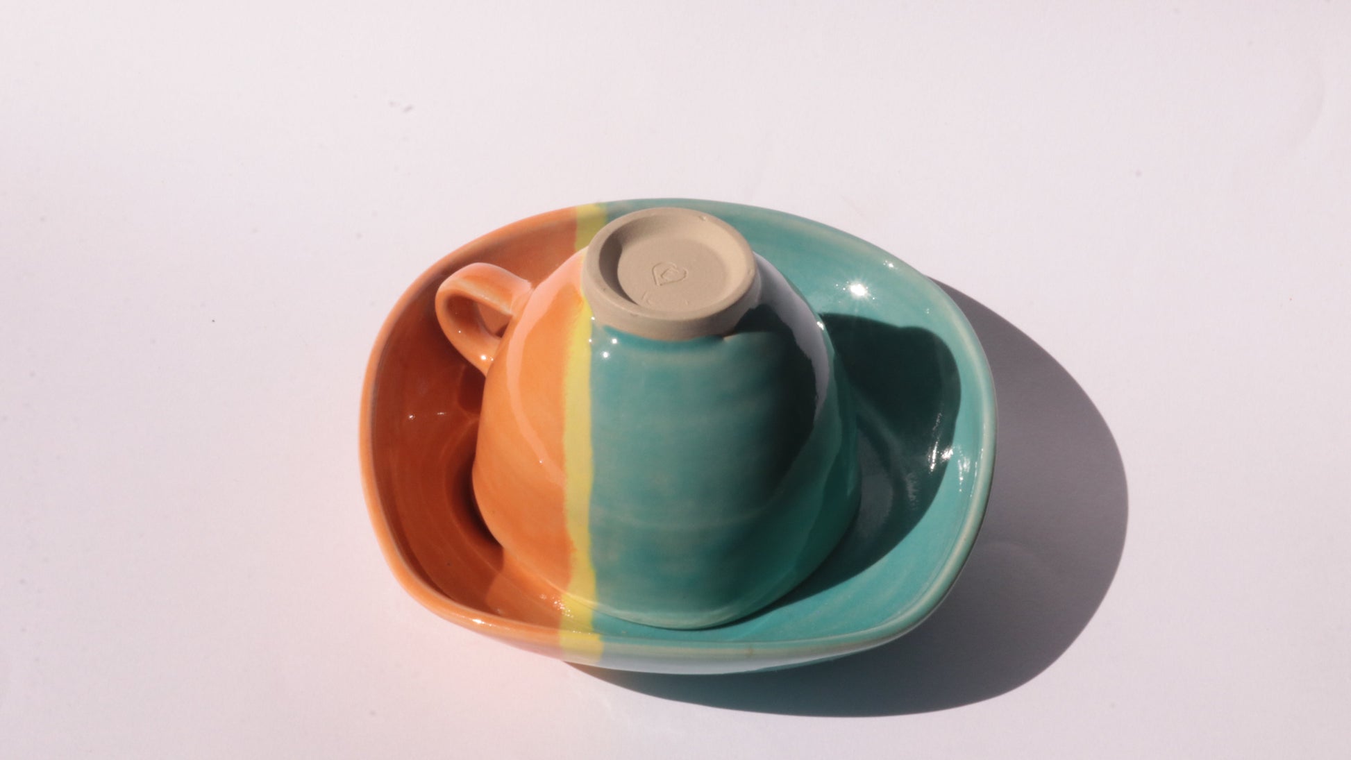 Teal and orange ceramic cup and saucer with yellow stripe on a white background