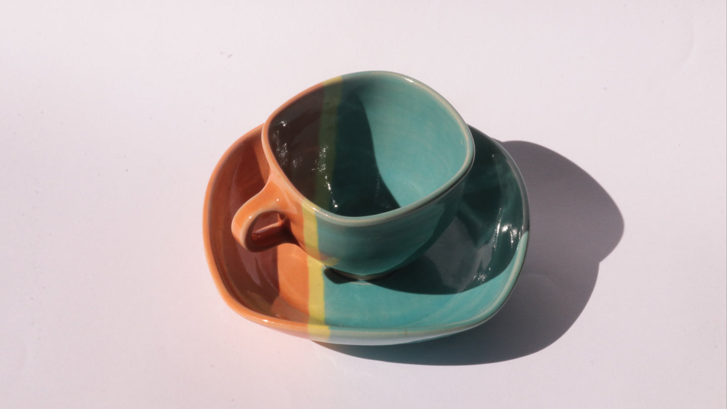 Teal and orange ceramic cup and saucer with yellow stripe on a white background