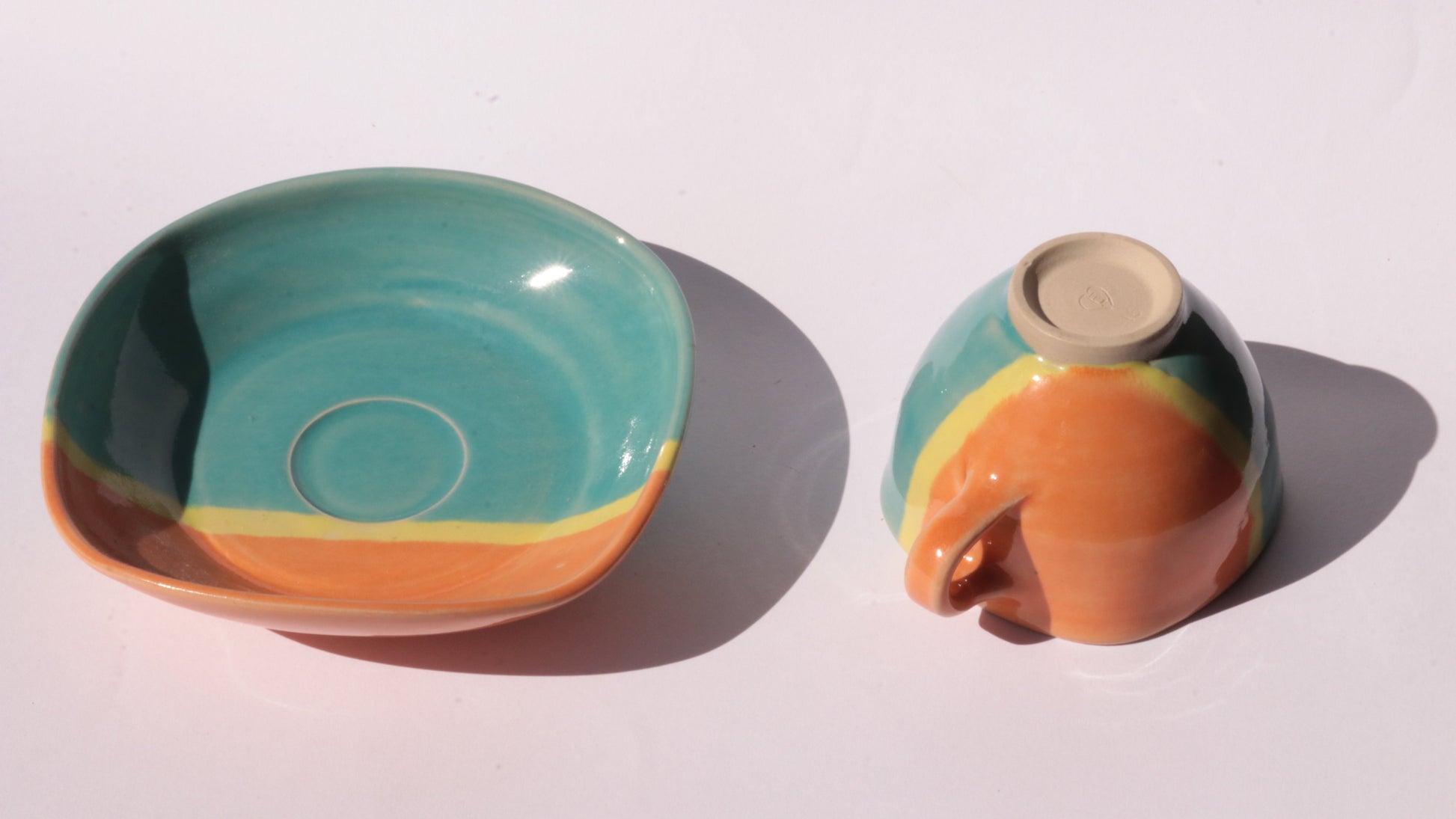 Teal and orange ceramic cup and saucer with yellow stripe on a white background