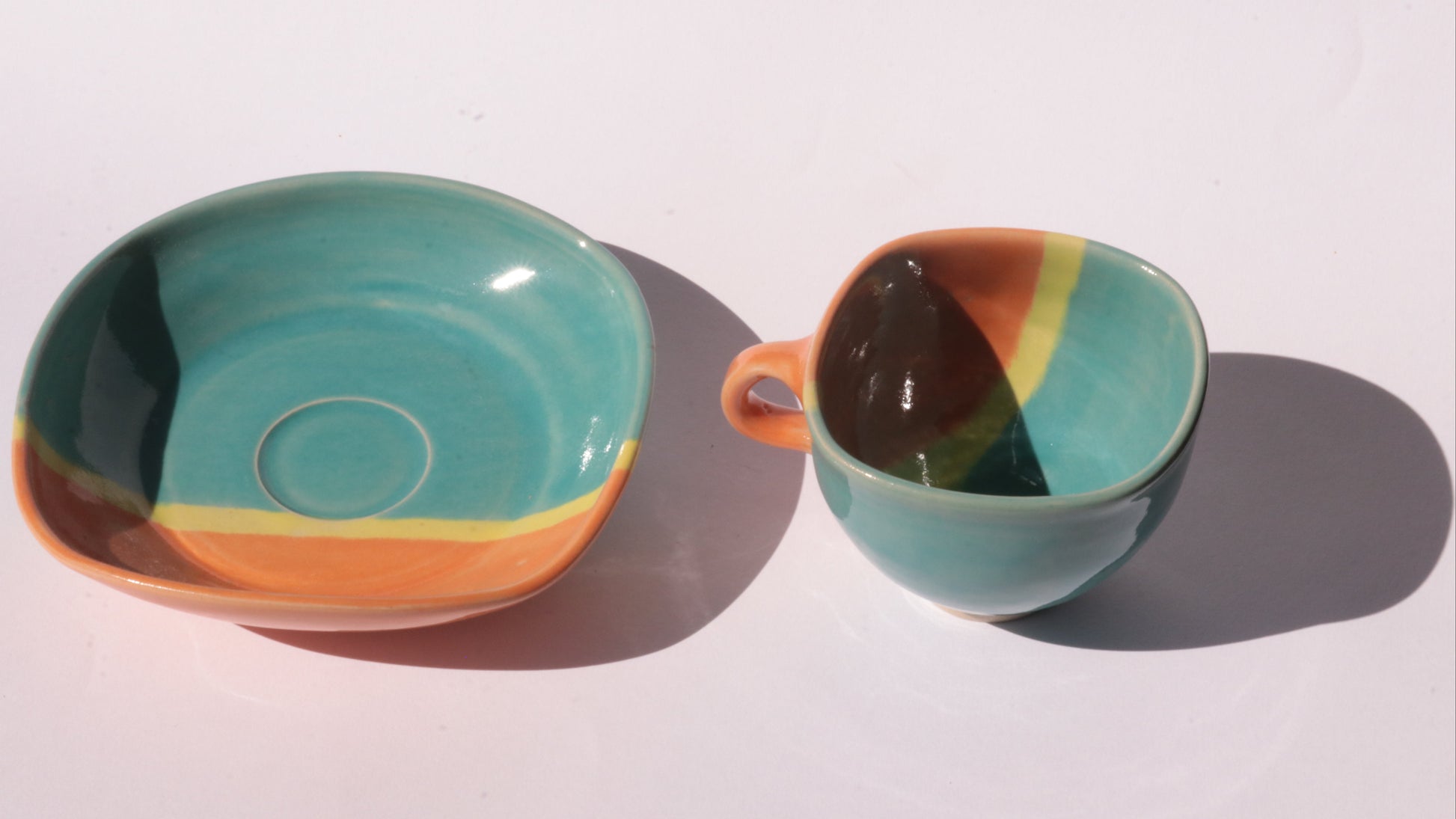 Teal and orange ceramic cup and saucer with yellow stripe on a white background