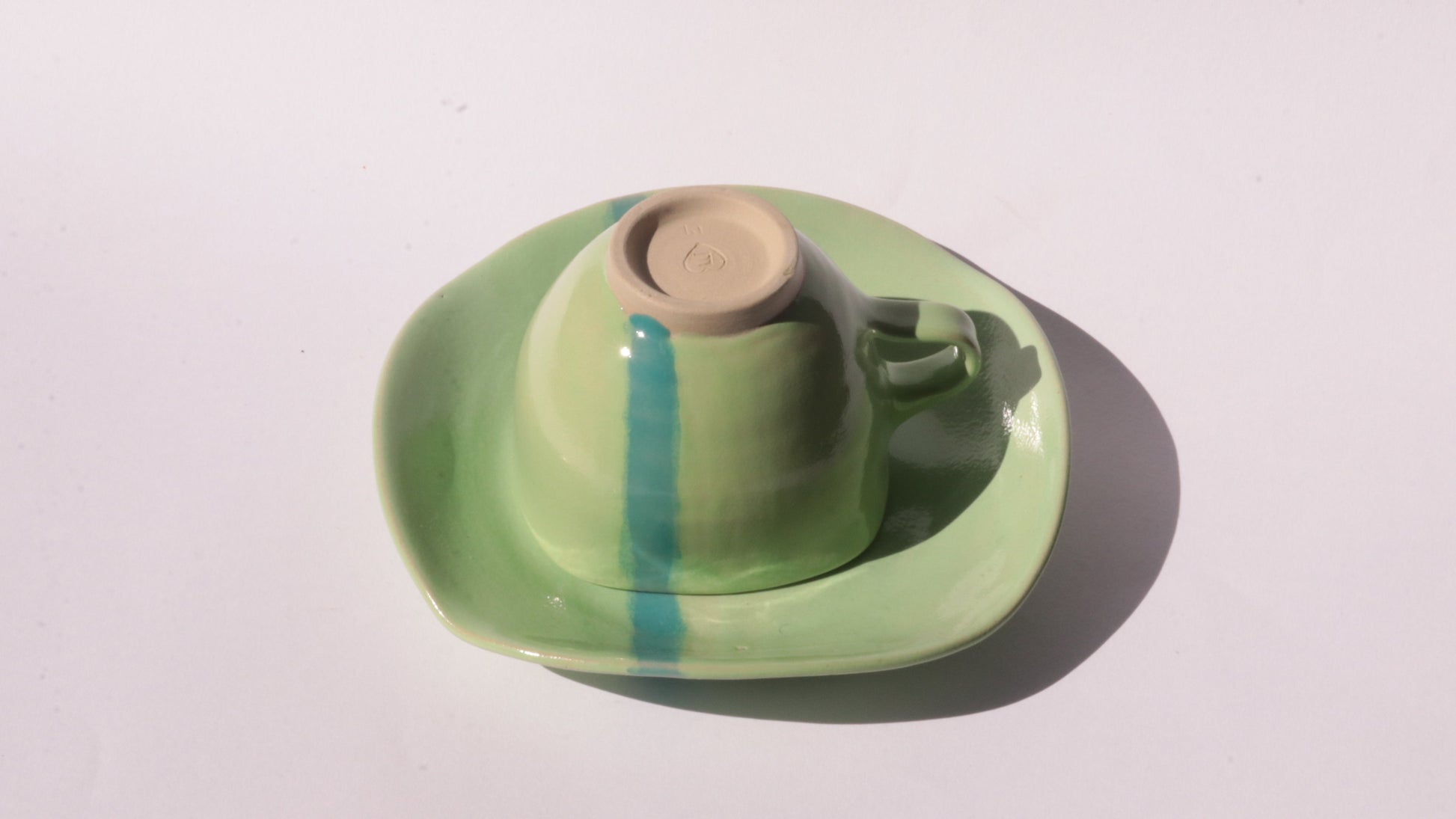 green ceramic cup and saucer with blue stripe on white background
