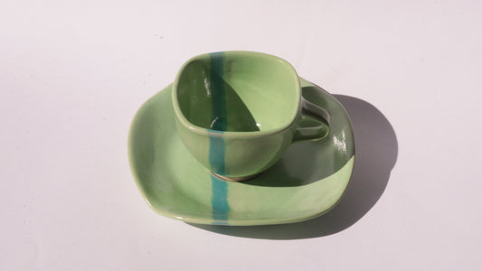 green ceramic cup and saucer with blue stripe on white background