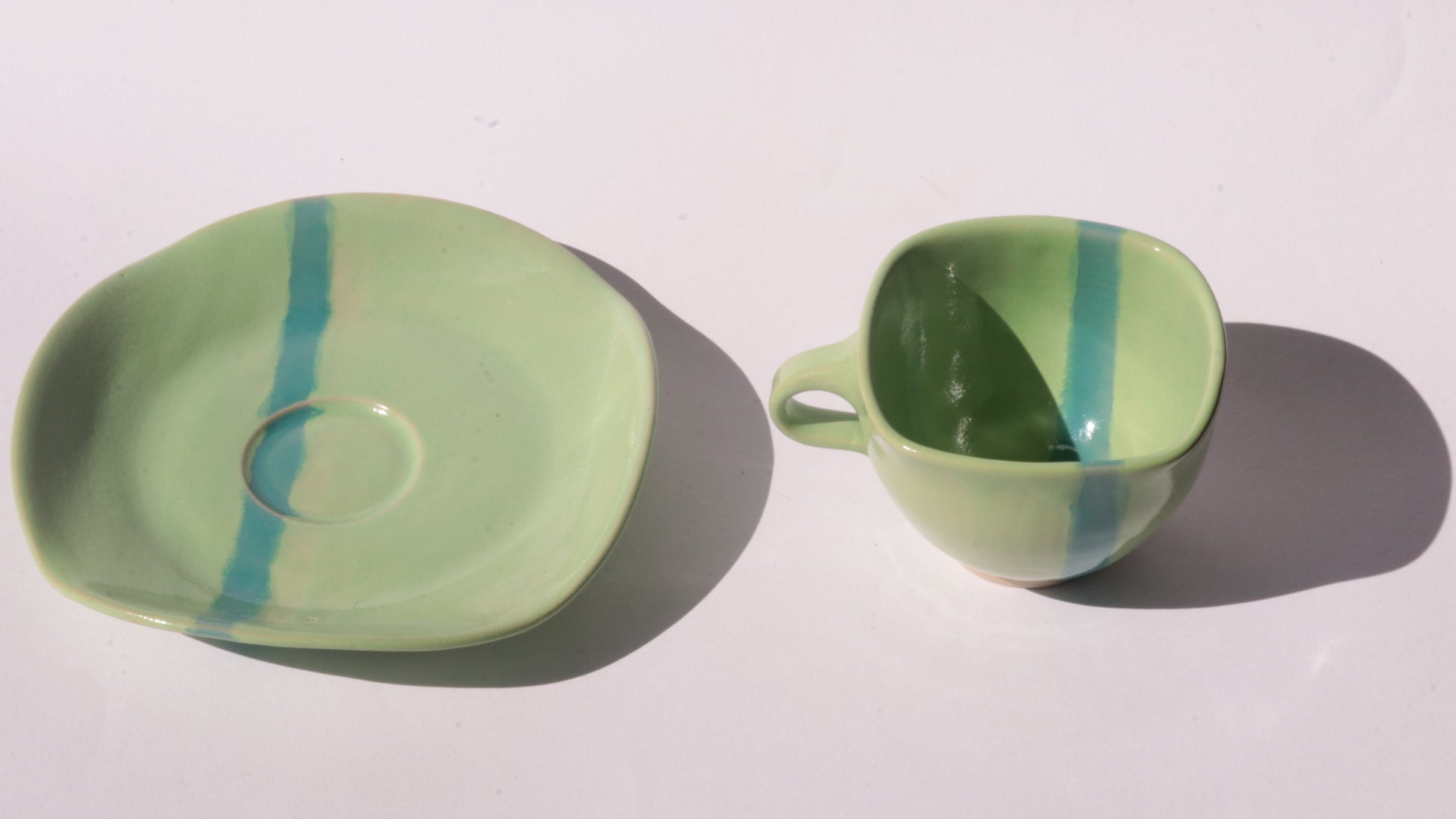 green ceramic cup and saucer with blue stripe on white background