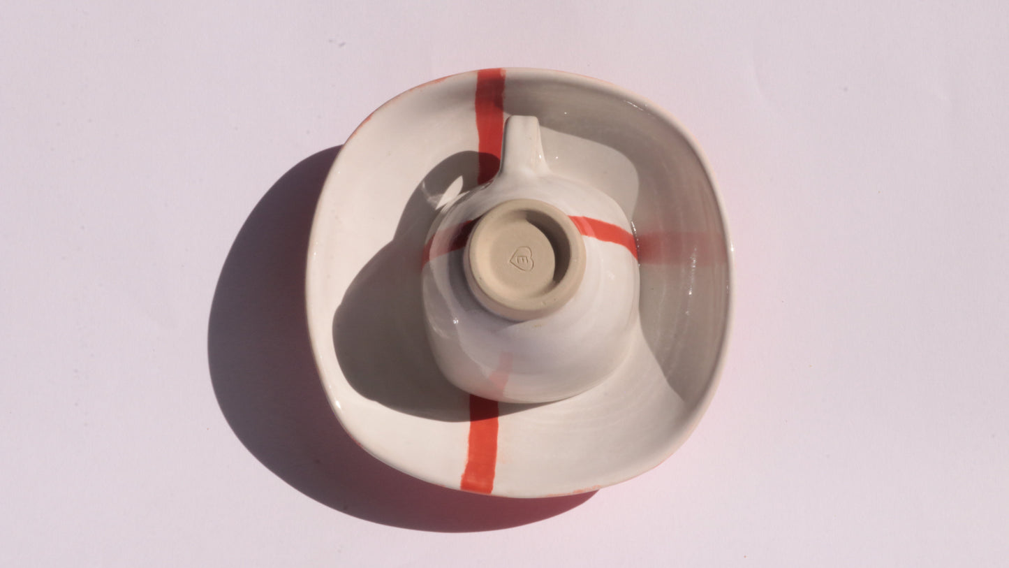 Ceramic cup and saucer with a red stripe on a white background
