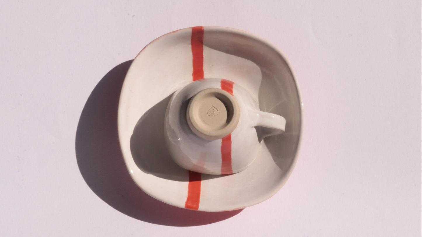 Ceramic cup and saucer with a red stripe on a white background