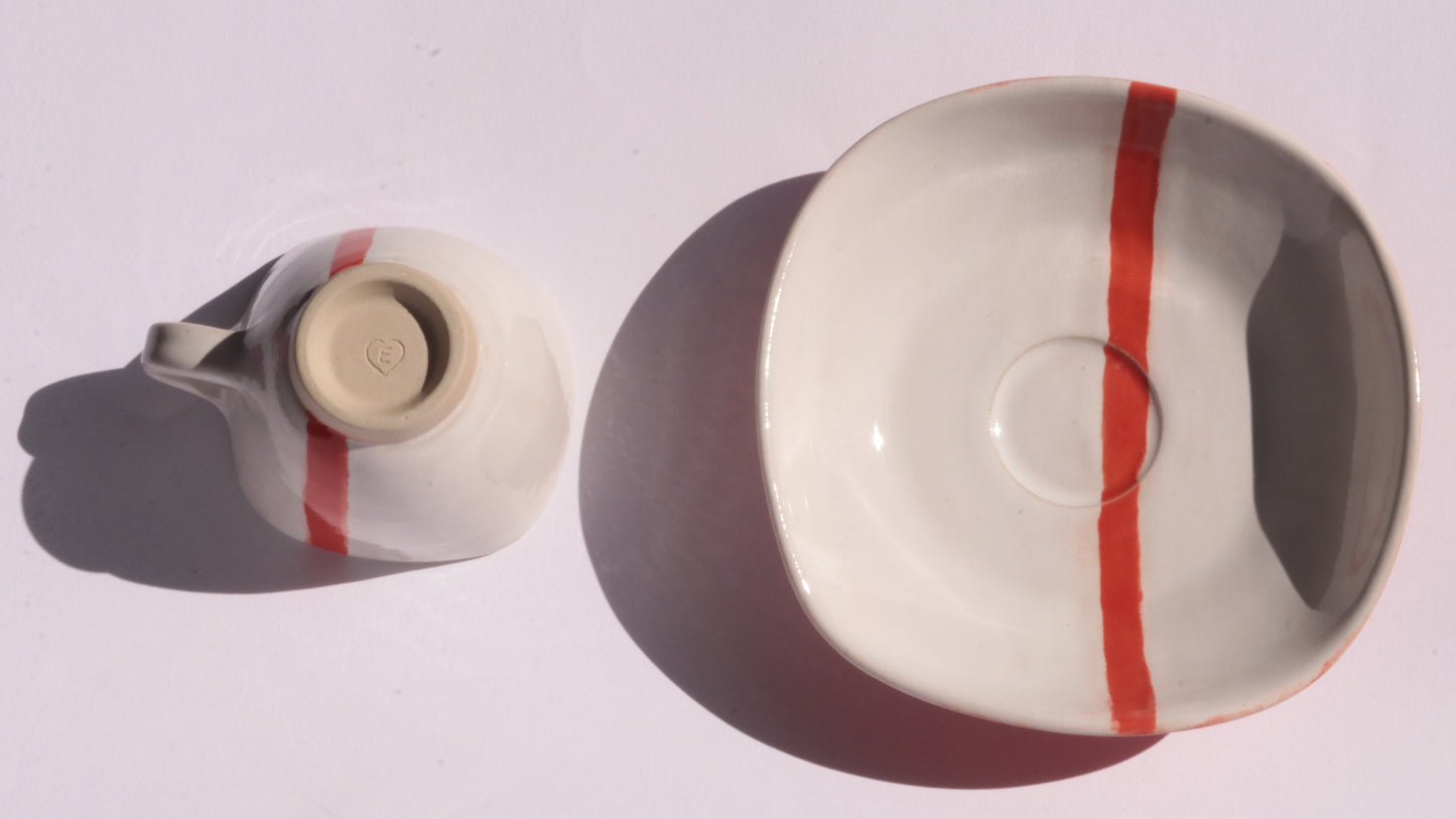 Ceramic cup and saucer with a red stripe on a white background