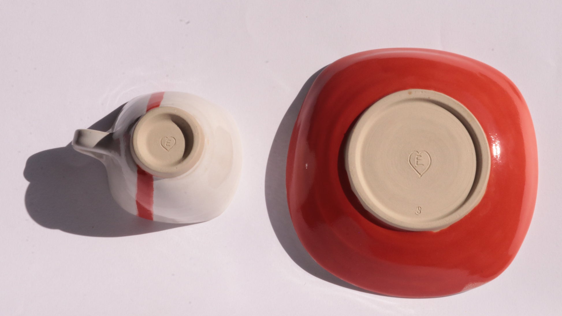 Ceramic cup and saucer with a red stripe placed upside down on a white background