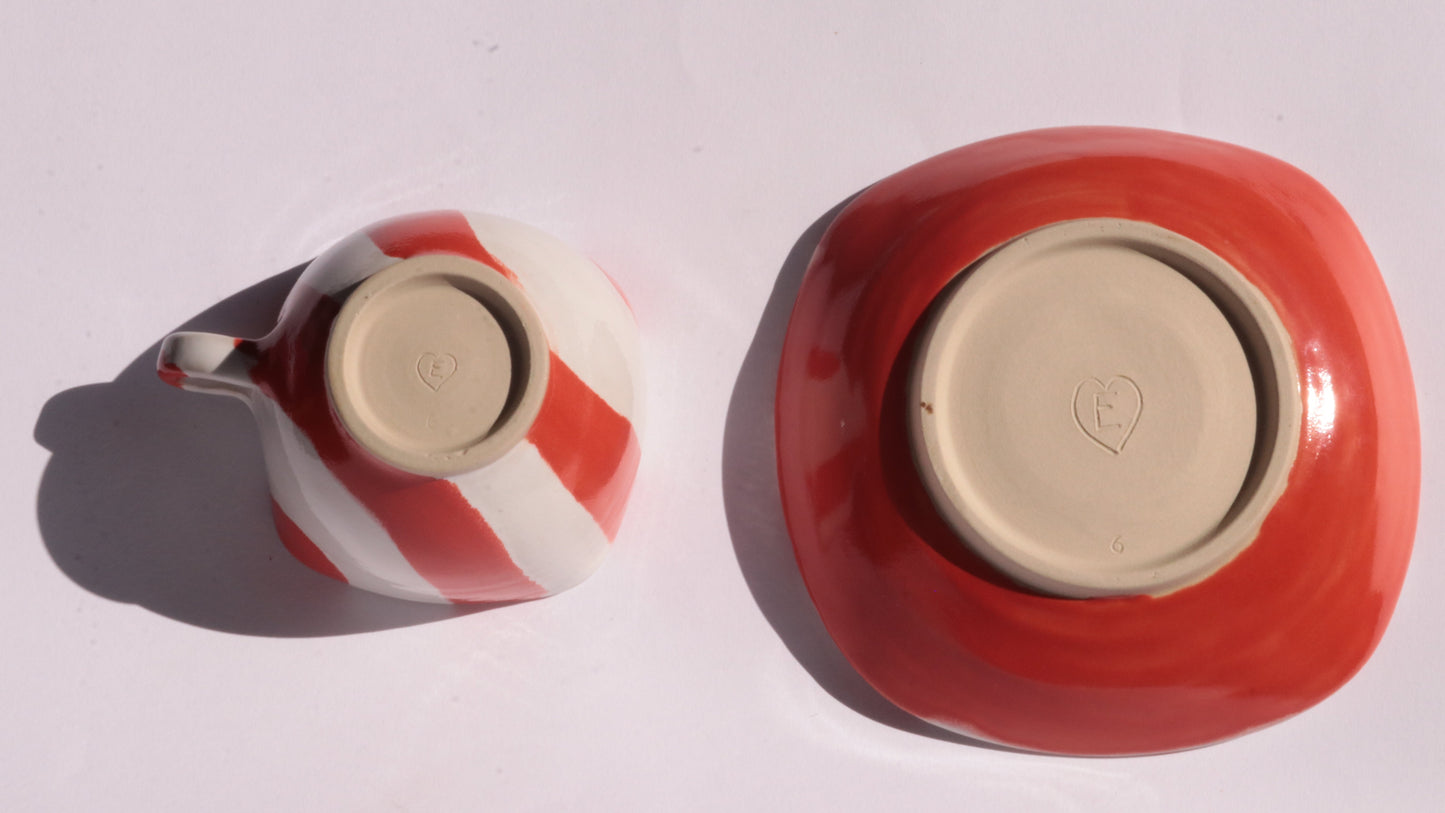 red and white striped ceramic cup and saucer placed upside down on white background