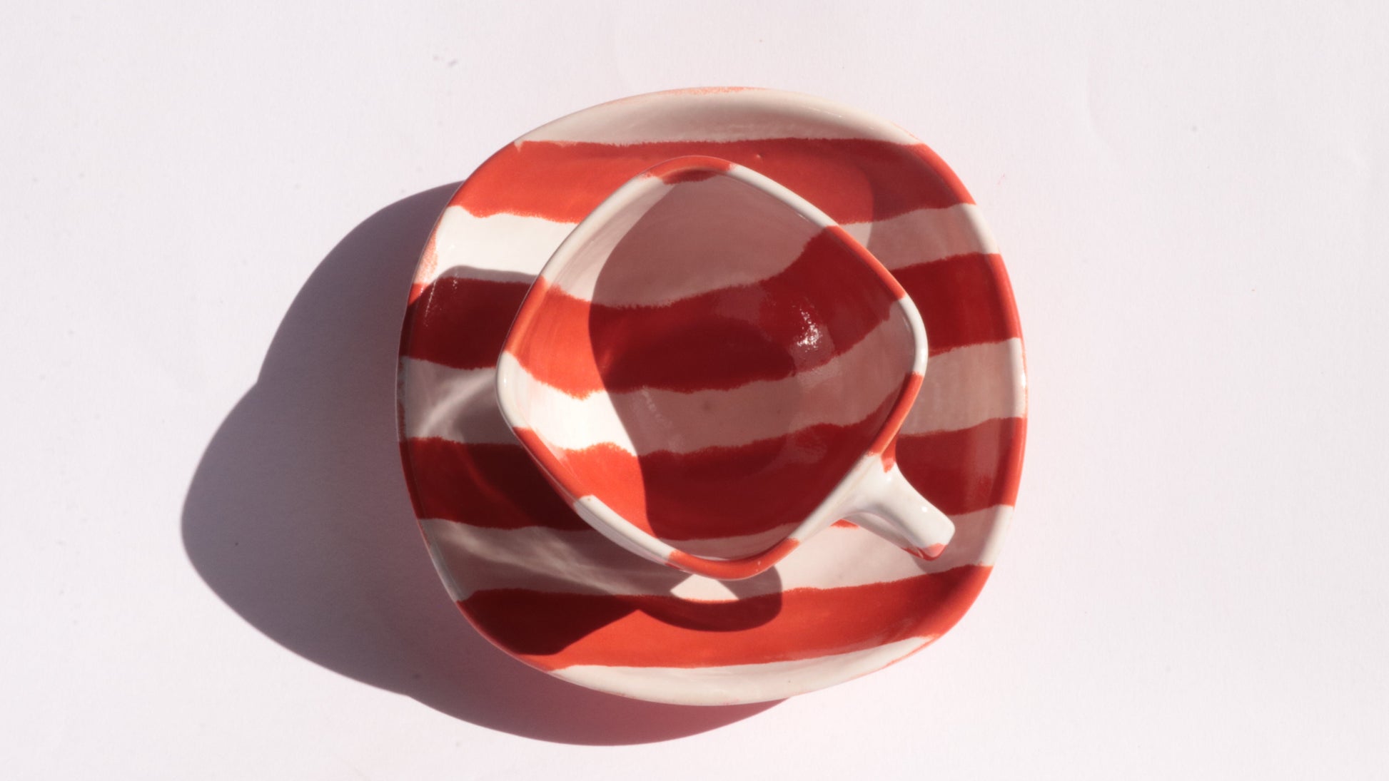 red and white striped ceramic cup and saucer on white background