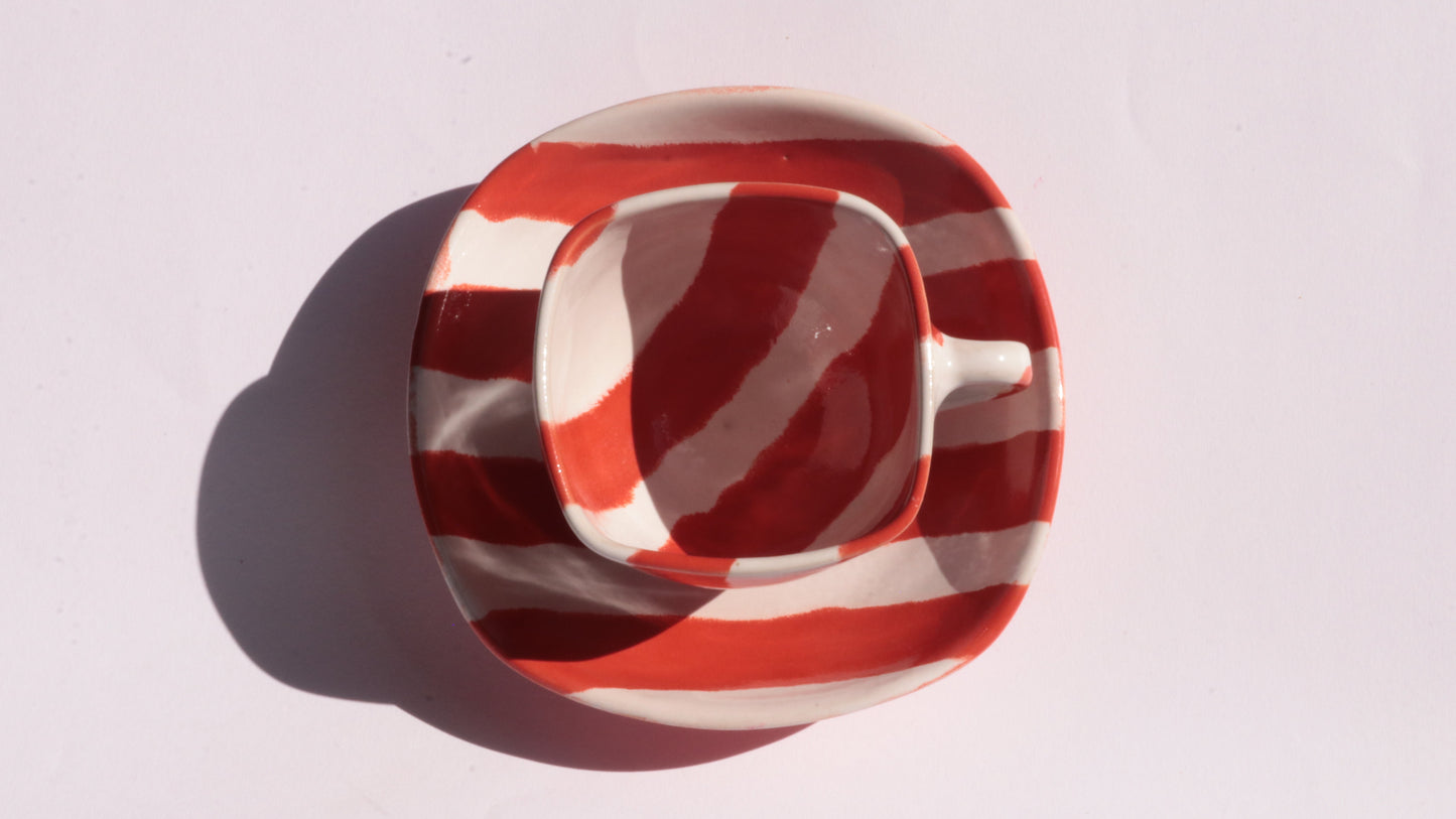 red and white striped ceramic cup and saucer on white background