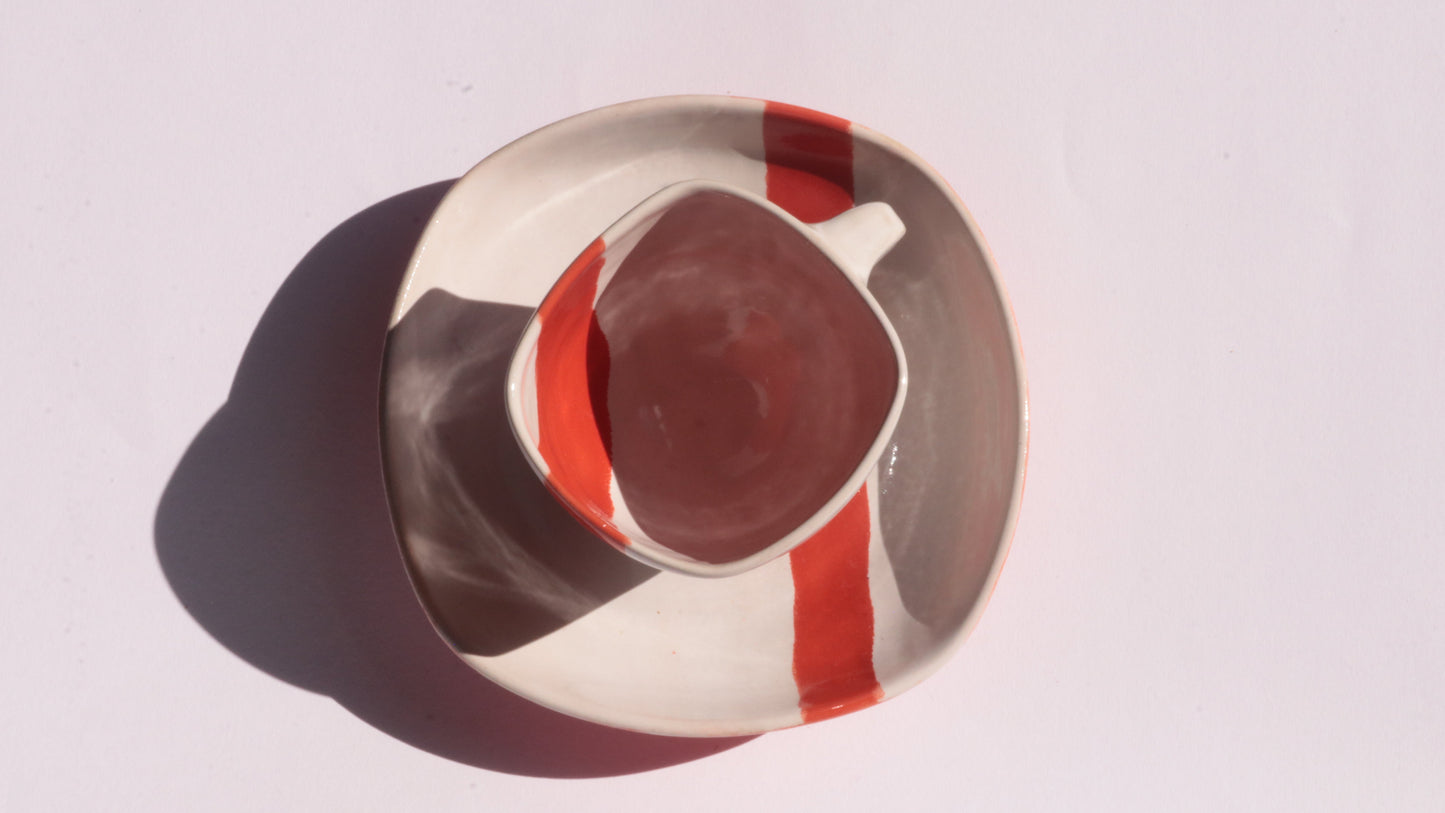 Ceramic cup and saucer with thick red stripe on a white background