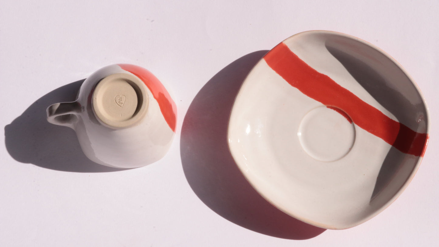 Ceramic cup and saucer with thick red stripe on a white background