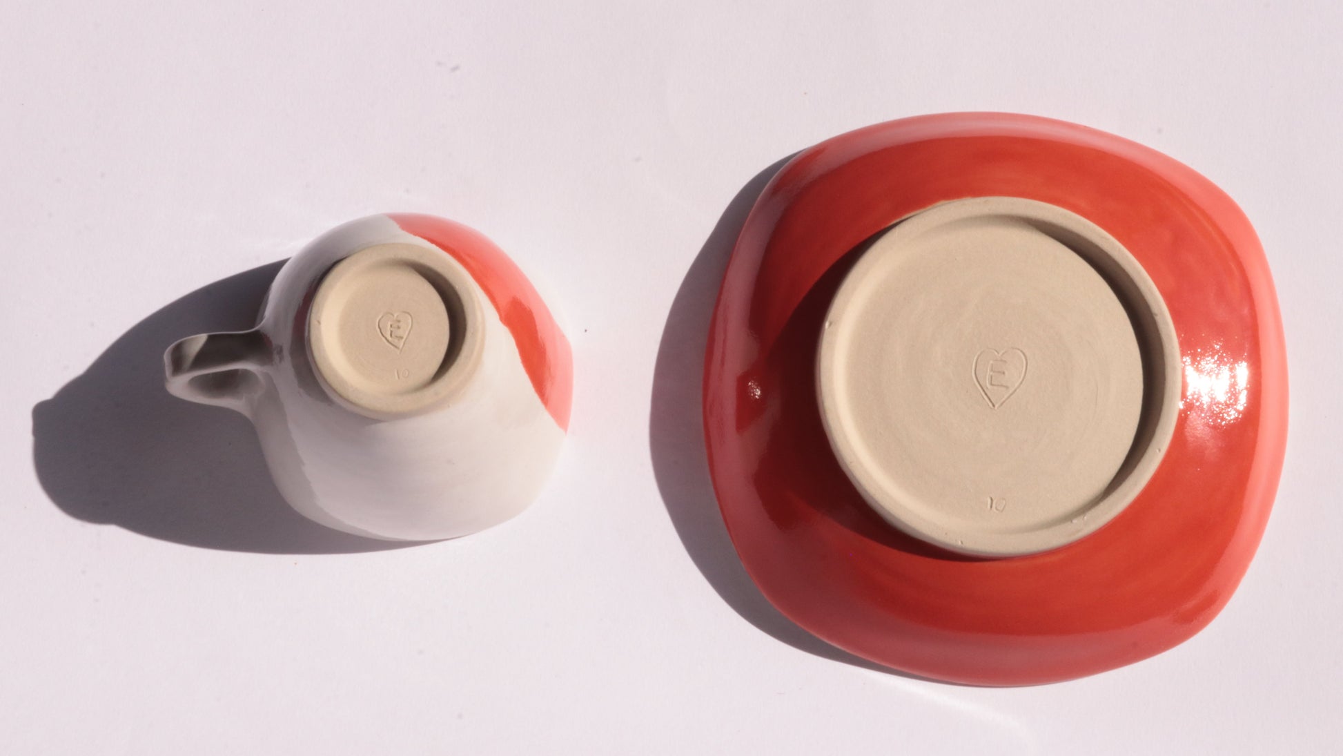 Ceramic cup and saucer with thick red stripe placed upside down on a white background