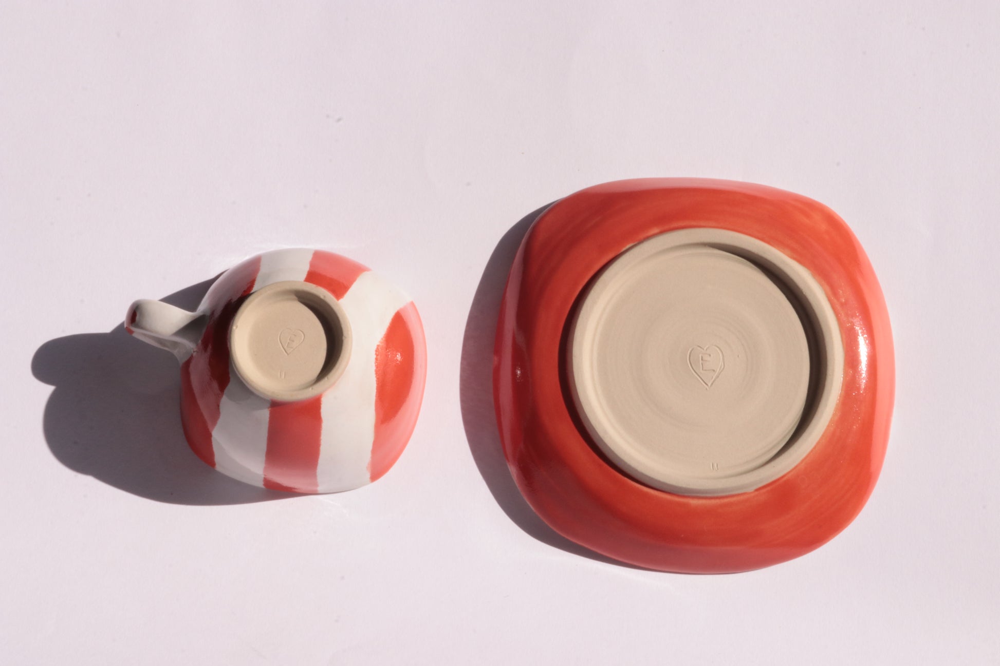 Ceramic cup and saucer with red and white stripe turned upside down on a white background