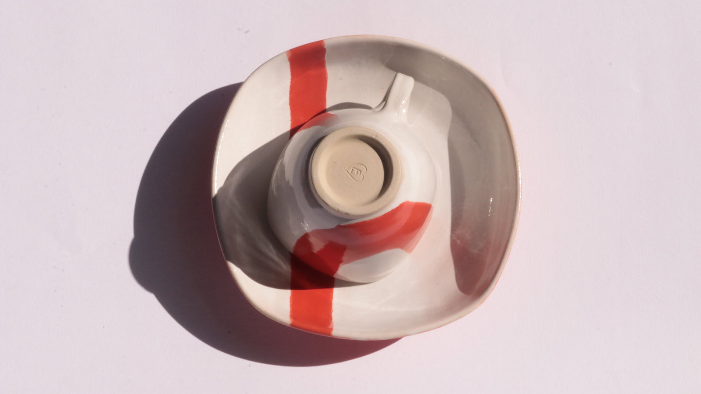 Ceramic cup and saucer with thick red stripe on a white background