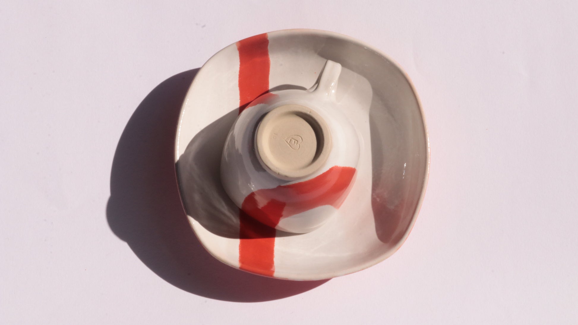 Ceramic cup and saucer with thick red stripe on a white background