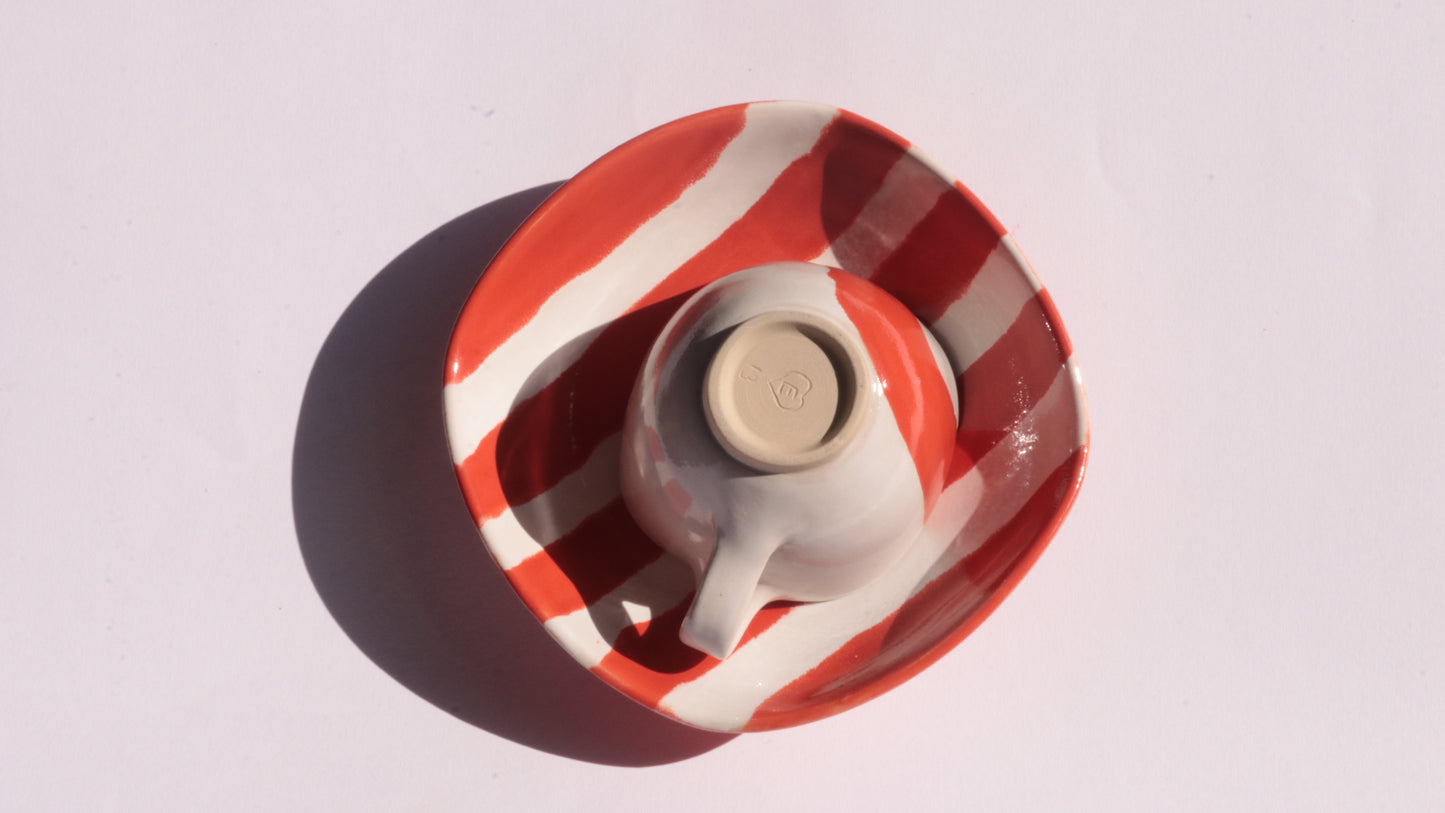 Ceramic cup and saucer with red and white stripes on a white background