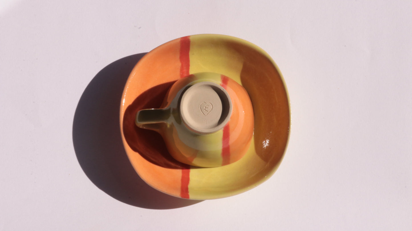 Ceramic cup and plate  with yellow, red, and orange stripes on a white background