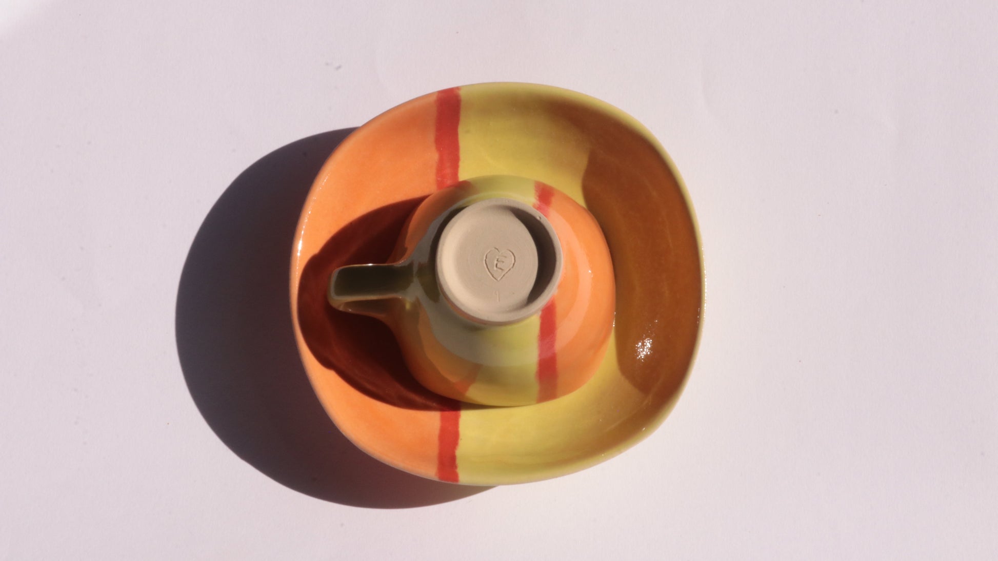 Ceramic cup and plate  with yellow, red, and orange stripes on a white background