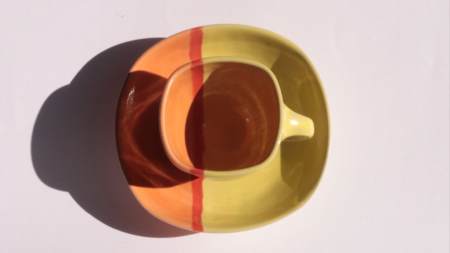 yellow and orange ceramic cup and saucer with red line on a white background