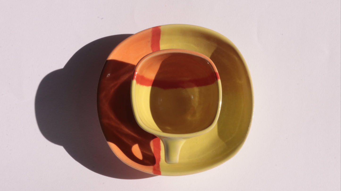 Colorful ceramic cup and saucer with  yellow, orange and red stripes on a white background