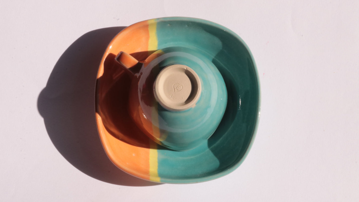 Teal and orange ceramic cup and saucer with yellow stripe on a white background