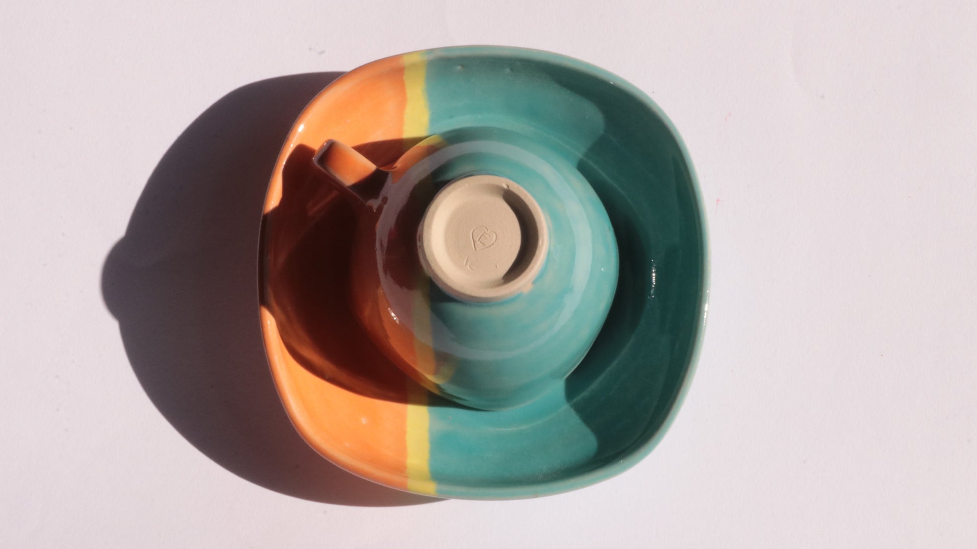 Teal and orange ceramic cup and saucer with yellow stripe on a white background